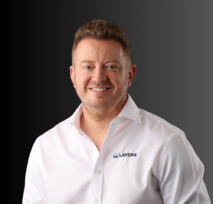 Smiling man in a white shirt with Layer 4 logo, representing the senior team at Layer 4, a managed IT services provider.